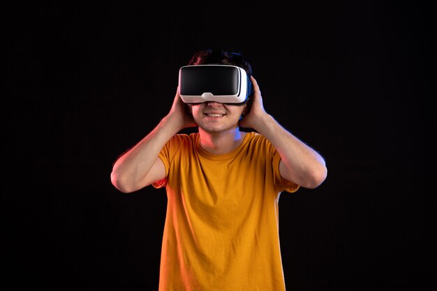 Vue de face d'un jeune homme portant un casque de réalité virtuelle sur un mur sombre