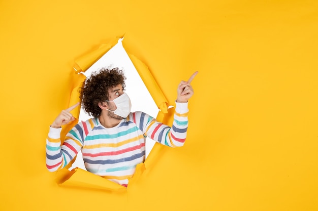 Photo gratuite vue de face jeune homme portant un masque stérile sur une photo de virus pandémique humain de couleur jaune déchirée