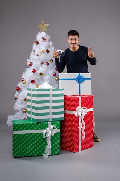 Vue de face jeune homme prenant une photo avec des cadeaux sur gris