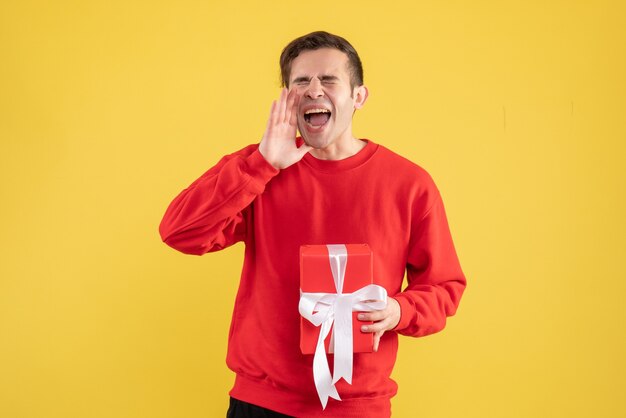 Vue de face jeune homme avec pull rouge criant sur l'espace de copie de fond jaune