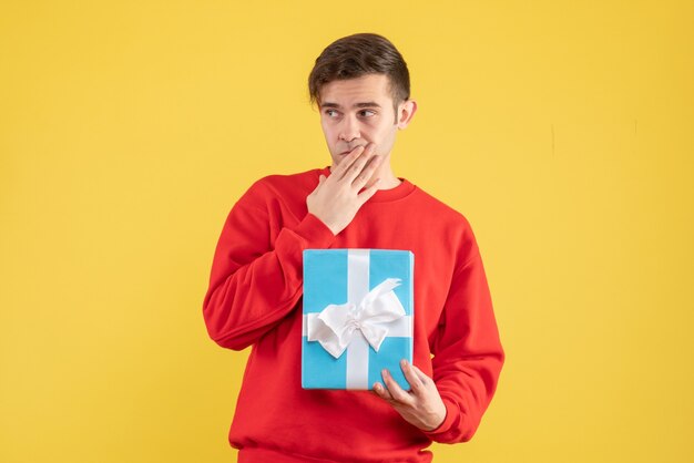 Vue de face jeune homme avec pull rouge debout sur fond jaune