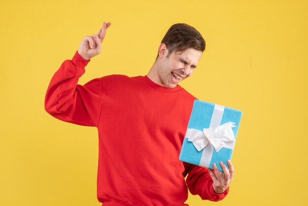 Vue de face jeune homme avec pull rouge faisant signe de bonne chance sur fond jaune