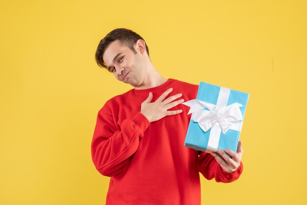 Vue de face jeune homme avec pull rouge mettant la main sur sa poitrine sur fond jaune