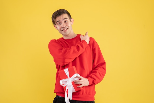 Vue de face jeune homme avec pull rouge pointant vers l'arrière sur fond jaune