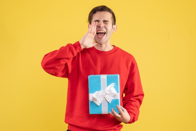 Vue de face jeune homme avec pull rouge saluant quelqu'un sur fond jaune