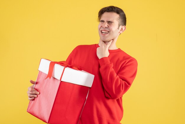 Vue de face jeune homme avec pull rouge tenant la gorge sur fond jaune