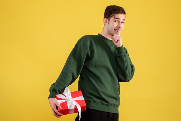 Vue de face jeune homme avec pull vert faisant signe chut debout sur jaune