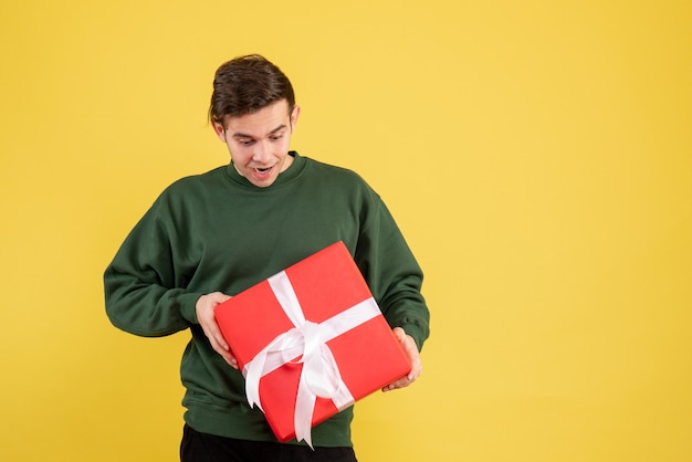 Vue De Face Jeune Homme Avec Pull Vert En Regardant Son Cadeau Sur Jaune