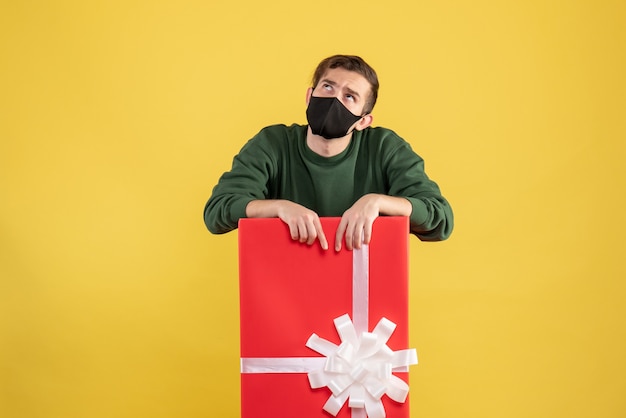 Vue de face jeune homme à la recherche debout derrière une grande boîte-cadeau sur jaune