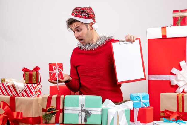 Vue de face jeune homme regardant cadeau assis autour de cadeaux de Noël