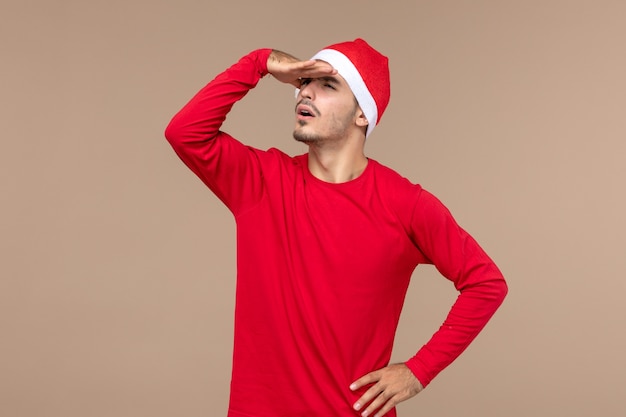 Vue de face jeune homme regardant à distance sur fond brun émotion de vacances de Noël