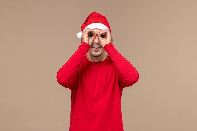 Vue de face jeune homme regardant à travers les doigts sur fond brun émotion de vacances de Noël