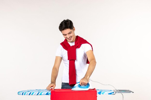Vue de face jeune homme repassage serviette rouge sur fond blanc homme travaux ménagers émotion accueil travail propre couleur de blanchisserie