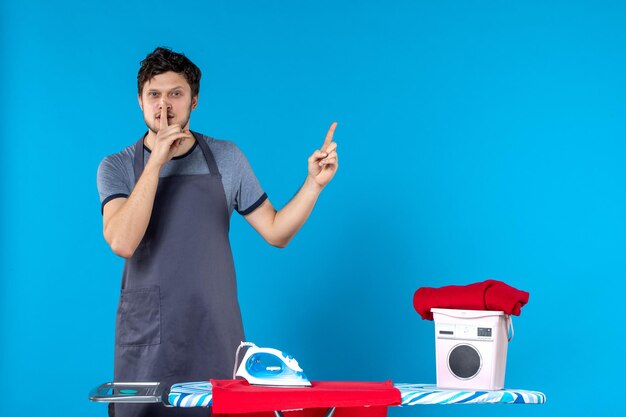 Vue de face jeune homme repassant une chemise rouge et la brûlant sur une surface bleue