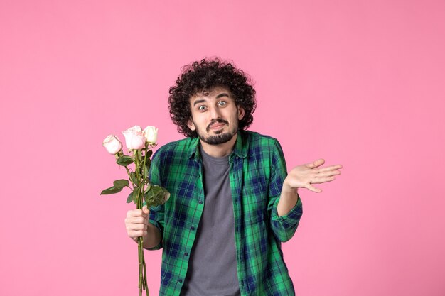 Vue de face jeune homme avec des roses roses comme cadeau pour la journée des femmes sur la couleur rose