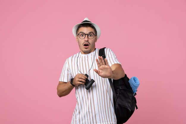 Vue de face jeune homme avec sac et jumelles sur fond rose