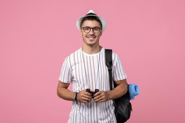 Vue de face jeune homme avec sac et jumelles sur fond rose