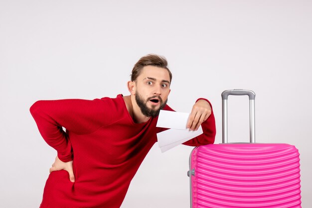 Vue de face jeune homme avec sac rose et tenant des billets sur un mur blanc couleur voyage vol voyage touriste