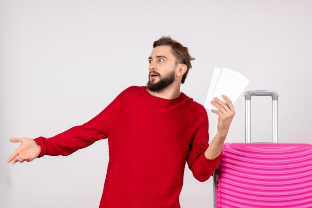 Vue de face jeune homme avec sac rose et tenant des billets sur le mur blanc vols couleur voyage voyage vacances touristiques