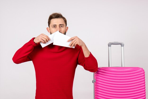 Vue de face jeune homme avec sac rose et tenant des billets sur un mur blanc voyage couleur voyage vacances émotion photo