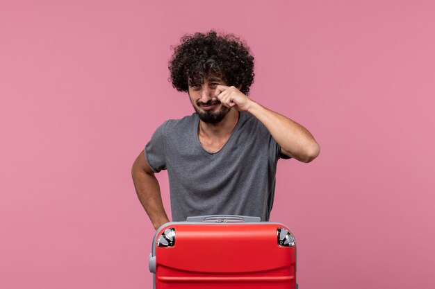 Vue de face jeune homme avec sac rouge se préparant au voyage en pleurant sur un espace rose