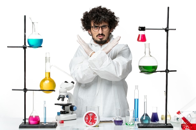 Vue de face jeune homme scientifique en costume spécial blanc montrant le signe d'interdiction sur le mur blanc science chimie pandémique laboratoire covid