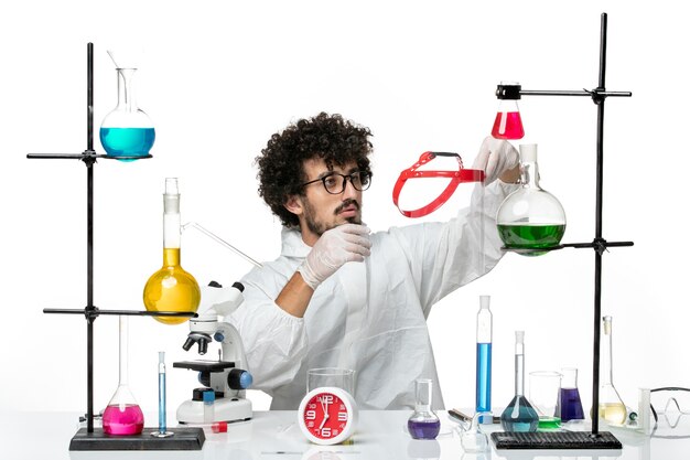 Vue de face jeune homme scientifique en costume spécial blanc tenant quelque chose sur le mur blanc science lab covid male chemistry