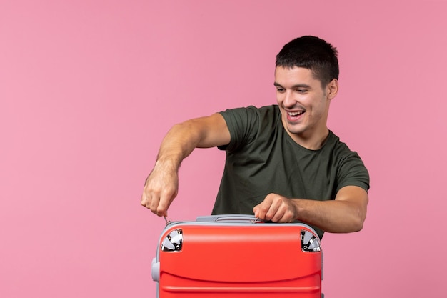 Vue de face jeune homme se préparant pour les vacances et fermant son sac sur un espace rose