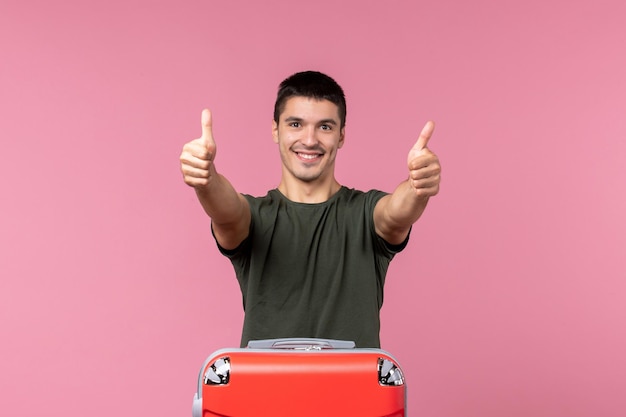 Vue de face jeune homme se préparant pour des vacances souriant sur un espace rose