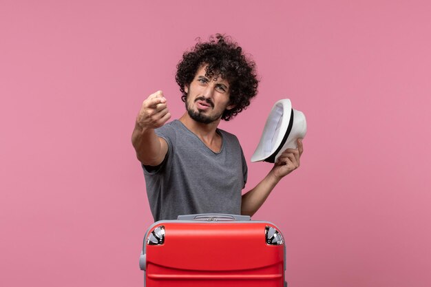 Vue de face jeune homme se préparant pour des vacances tenant un chapeau sur l'espace rose