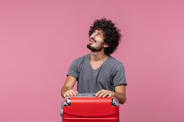 Vue de face jeune homme se préparant pour un voyage en avion sur un bureau rose