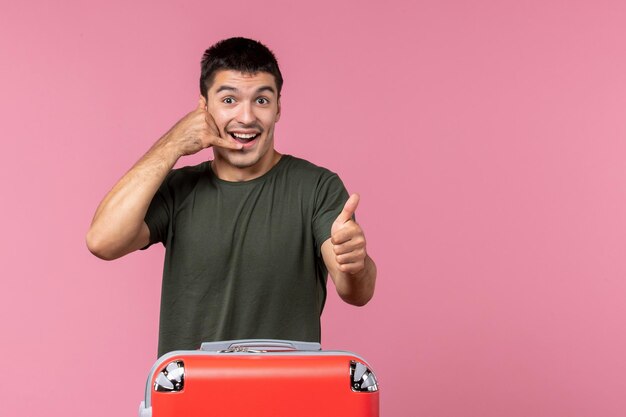 Vue de face jeune homme se préparant pour un voyage avec un sac rouge sur un espace rose