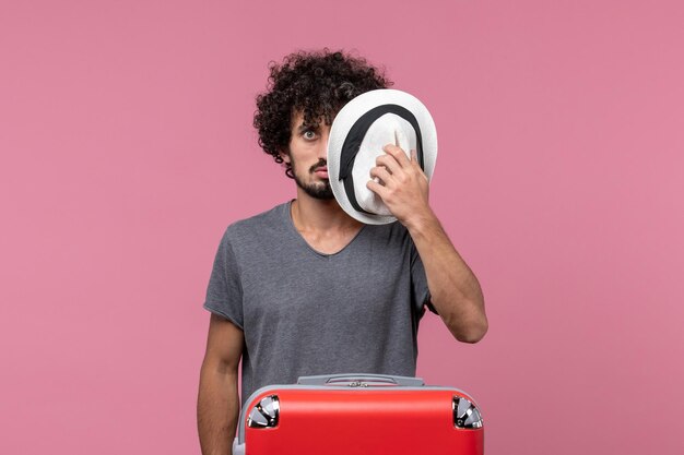 Vue de face jeune homme se préparant pour le voyage et tenant un chapeau sur l'espace rose