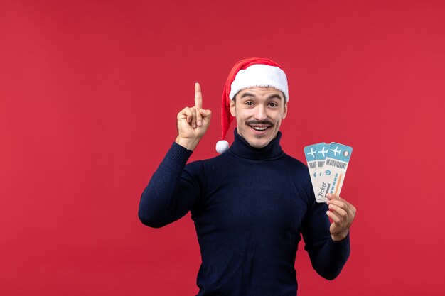 Vue de face jeune homme souriant avec des billets d'avion sur fond rouge