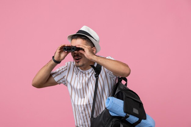 Vue de face jeune homme en t-shirt blanc à l'aide de jumelles sur fond rose