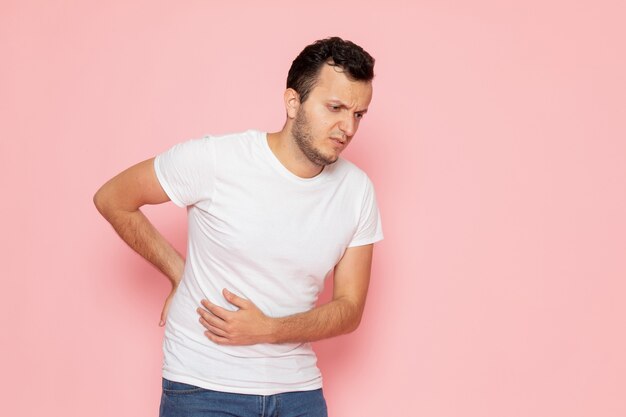 Une vue de face jeune homme en t-shirt blanc ayant un mal de ventre sur le bureau rose homme couleur émotion pose