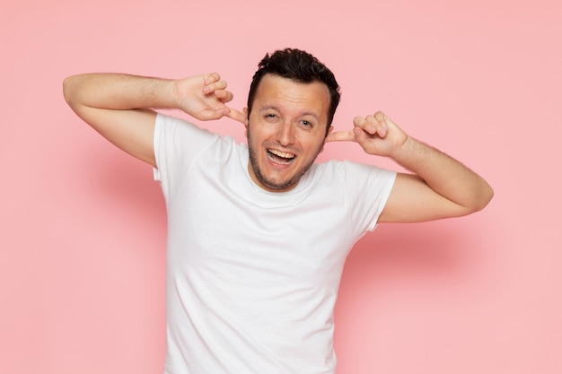 Une vue de face jeune homme en t-shirt blanc couvrant ses oreilles sur le bureau rose homme couleur émotion pose