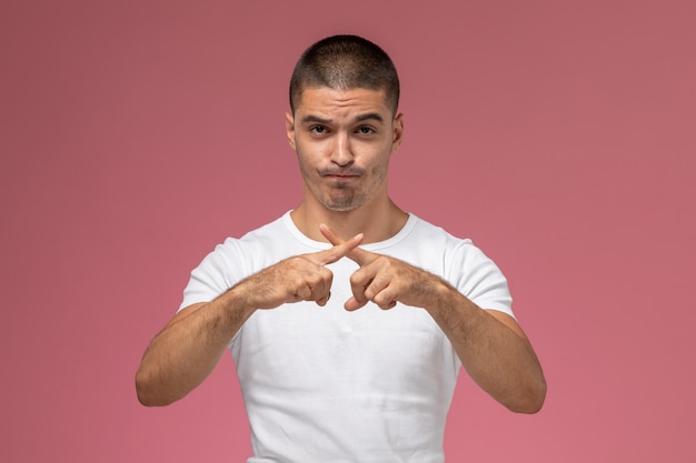 Vue de face jeune homme en t-shirt blanc croisant ses doigts sur fond rose