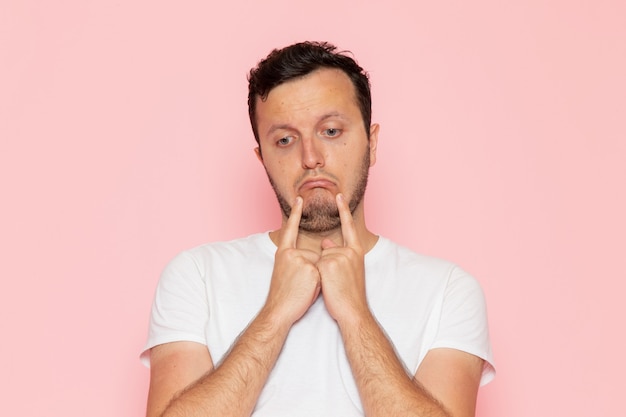 Une vue de face jeune homme en t-shirt blanc avec une expression attristée sur le bureau rose homme couleur émotion pose