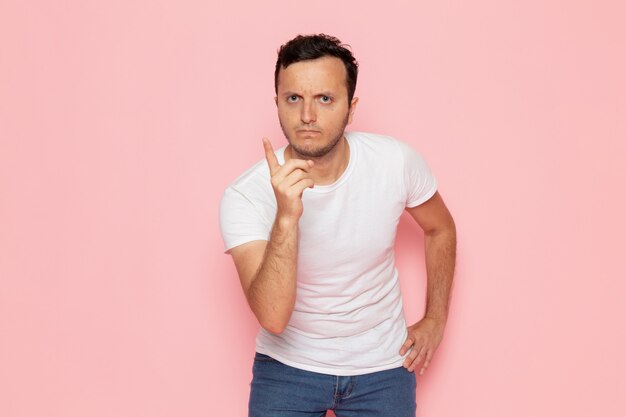 Une vue de face jeune homme en t-shirt blanc et jean bleu menaçant sur le bureau rose homme couleur émotion pose