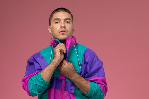 Vue de face jeune homme en t-shirt blanc et manteau coloré posant la fermeture de son manteau sur fond rose