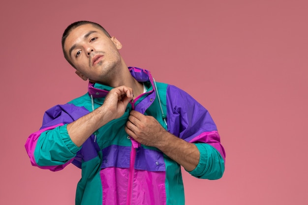 Vue de face jeune homme en t-shirt blanc et manteau coloré posant sur fond rose