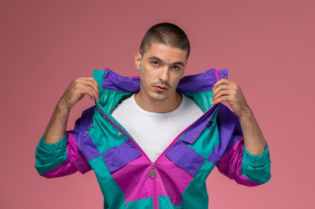 Vue de face jeune homme en t-shirt blanc et manteau coloré posant et montrant ses vêtements sur fond rose