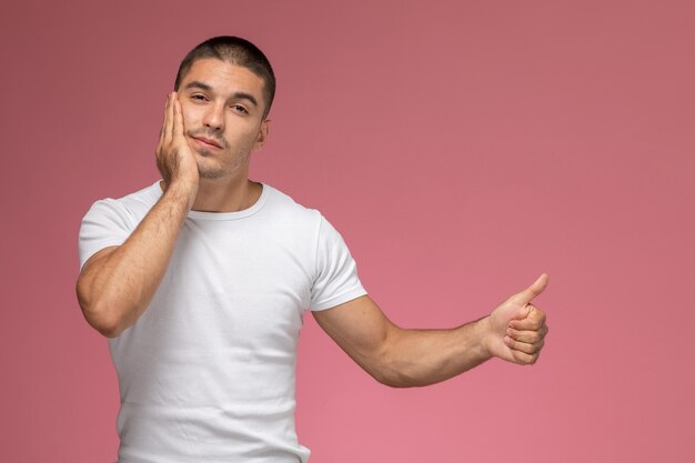 Vue de face jeune homme en t-shirt blanc posant ayant mal aux dents sur fond rose