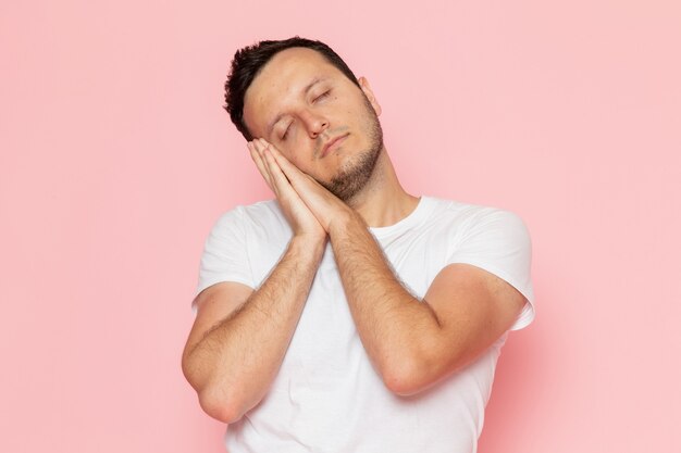 Une vue de face jeune homme en t-shirt blanc posant avec une douce expression de sommeil