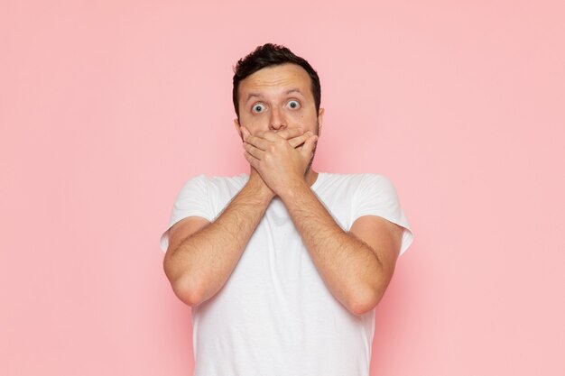 Une vue de face jeune homme en t-shirt blanc posant avec une expression choquée