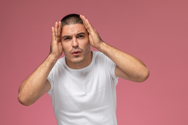 Vue de face jeune homme en t-shirt blanc posant avec une expression confuse sur un bureau rose