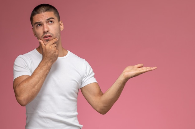 Vue de face jeune homme en t-shirt blanc posant avec expression de pensée sur fond rose