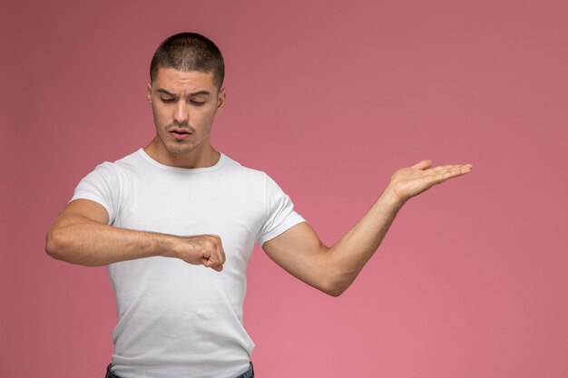 Vue de face jeune homme en t-shirt blanc en regardant son poignet sur le fond rose