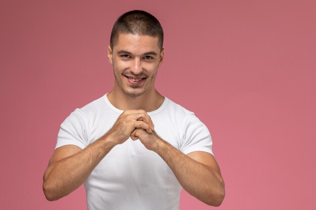 Vue de face jeune homme en t-shirt blanc souriant et serrant ses poings sur fond rose